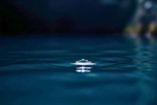 Fotografia macro e artística de águas profundas em tom escuro, com um leve reflexo de luz na superfície, representando o mergulho interno e a presença consciente no Tantra.